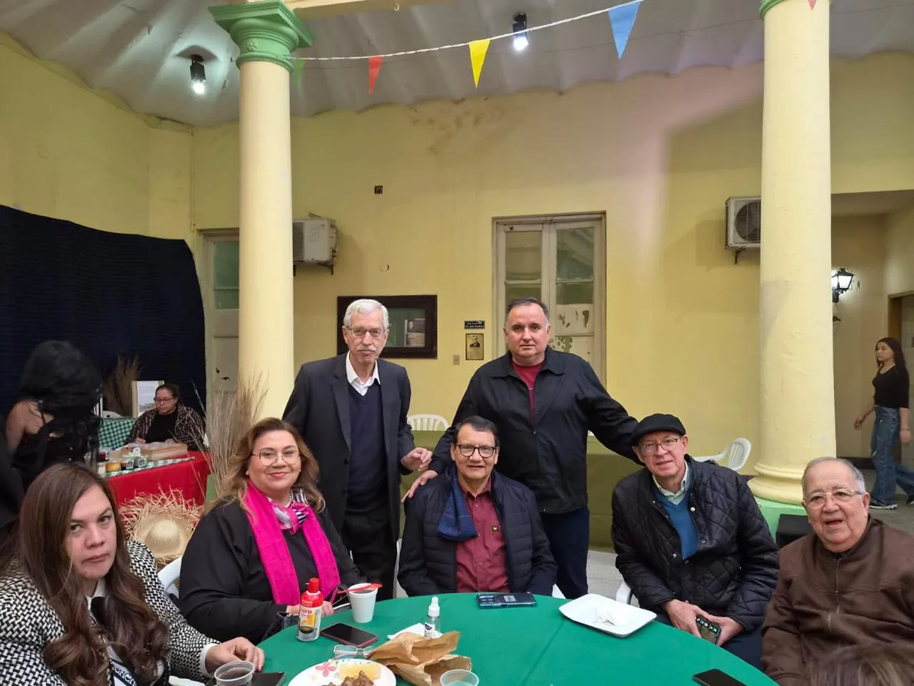 Socios y familiares compartiendo la mesa en el patio de la sede, bajo los banderines de la fiesta