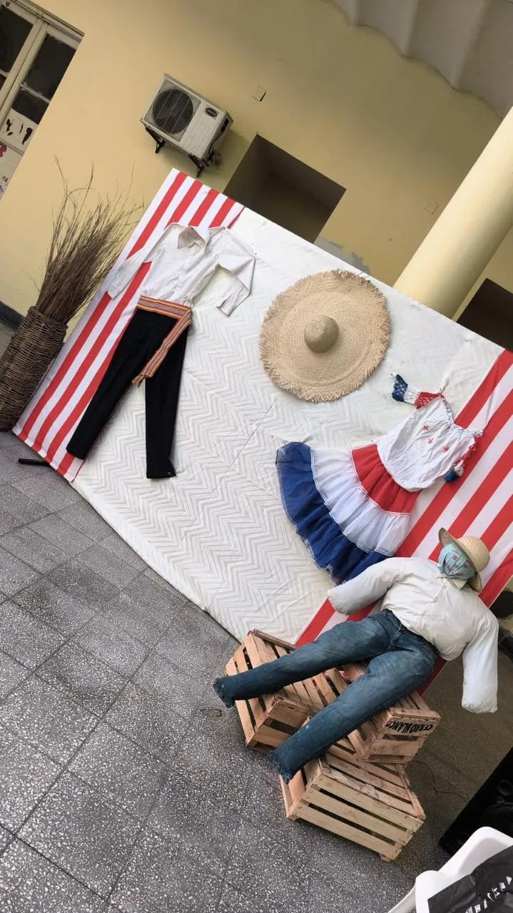 Rincón fotográfico con ropa típica paraguaya colgada y un muñeco de San Juan sentado sobre cajones de madera