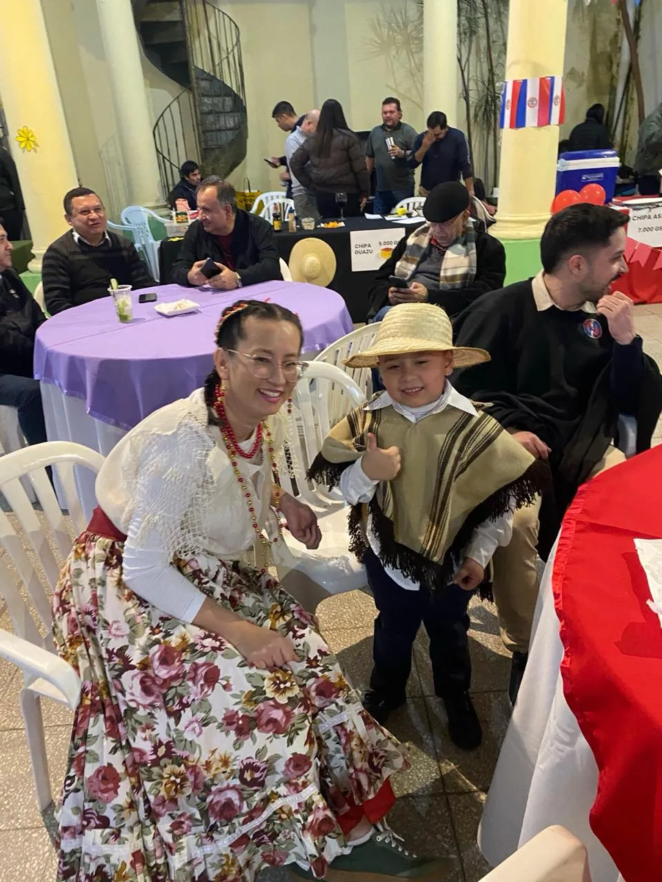 Una asistente con vestido típico y un niño con poncho y sombrero de paja, junto a los puestos de comida